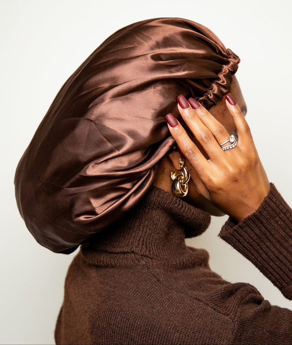 Person wearing a brown satin bonnet and matching sweater against a white background